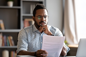 middle aged black man reviewing paperwork and holding his chin with his hand